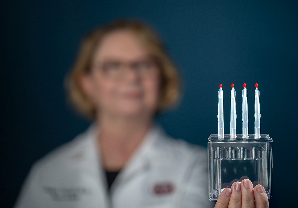 Jennifer Van Eyk, PhD, Director of Basic Science Reesearch holding a plastic container protecting four small sticks with rigid.