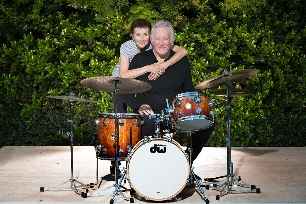 Denny Seiwell sitting behind his drum kit with wife Monique.