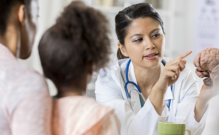 Woman doctor pointing to a brain model to a woman and child.