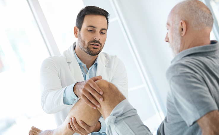 Doctor examining an older man's knee.
