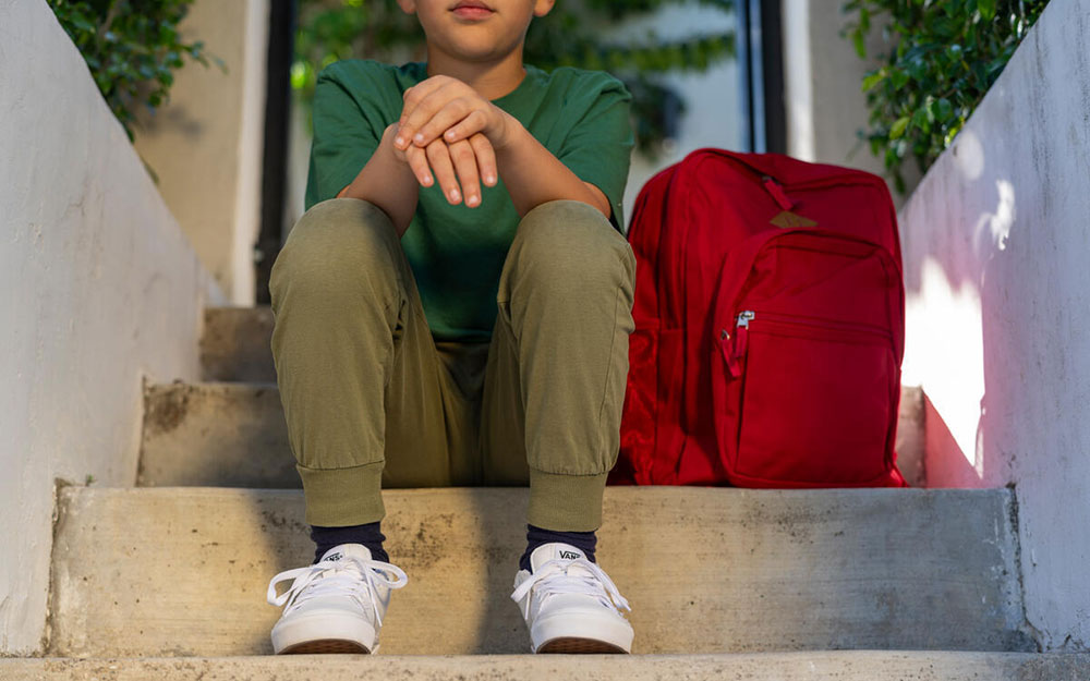 Child sitting on step with his shcool bag.