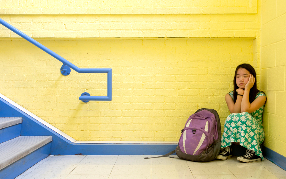 A child looking depressed sitting alone in a hallway at school. 