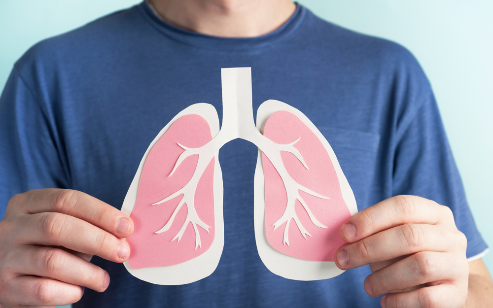 A man holding paper cutouts of lungs over his chest.