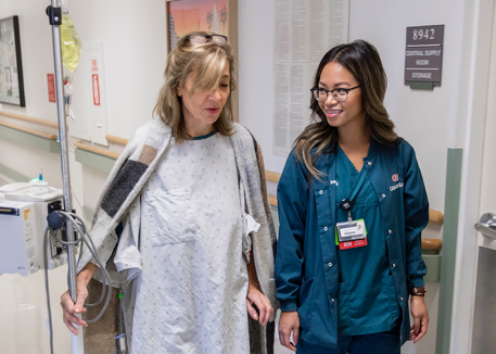Cedars-Sinai Nurse walking with patient down hospital hall.