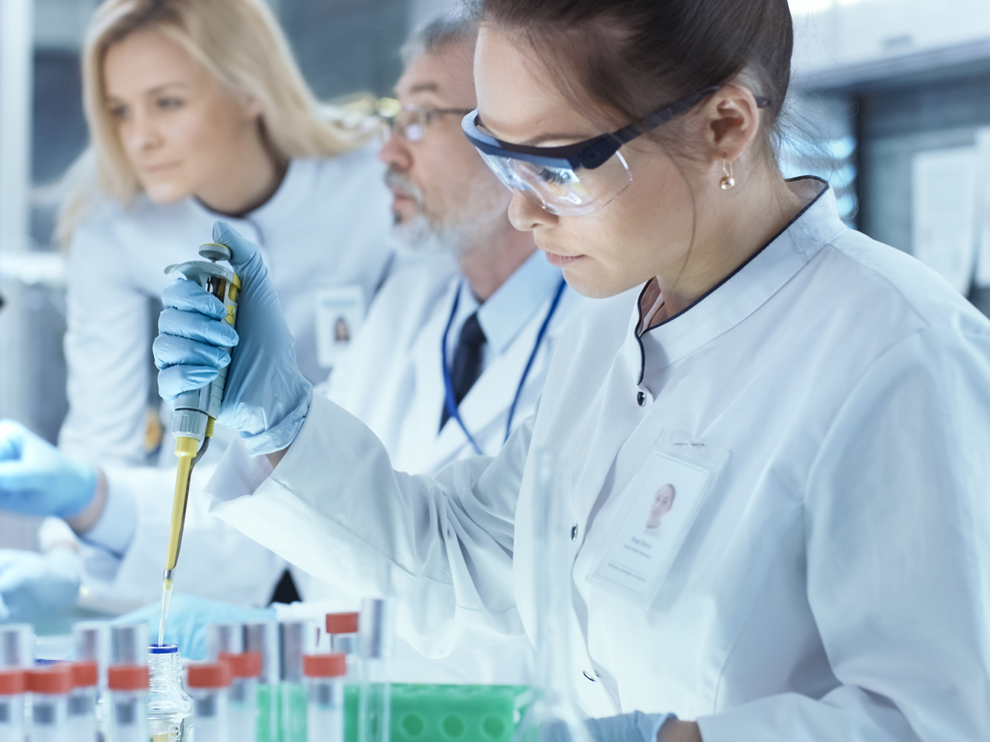Team of Research Scientists Working With Personal Computer, Analysing Test Trial New Generation Drug Data and Using Micropipette for Filling Test Tubes. They Work in a Modern Laboratory/ Medical Center.